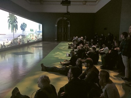 Exhibition visitors watching Lisa Reihana’s In Pursuit of Venus [infected] (2015–17; Auckland Art Gallery Toi o Tāmaki, gift of the Patrons of the Auckland Art Gallery, 2014). Installation view, Oceania, Royal Academy, 2018. Photo: Peter Brunt