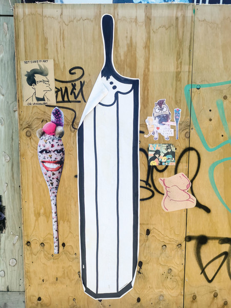 A large Teeth Like Screwdrivers pencil and a Vez spoon are surrounded by other paste-ups in the central city.